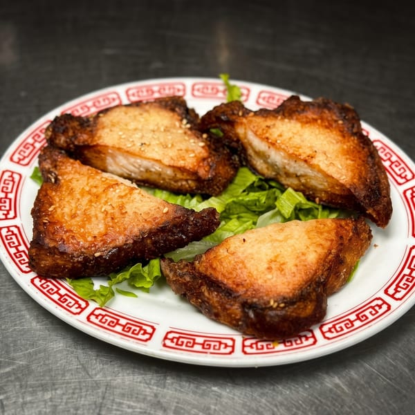 Four pieces of crispy shrimp toast with sesame seeds, served on lettuce on a white and red plate.