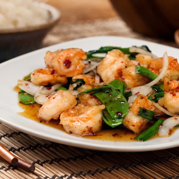 Shrimp stir-fry with green beans, onions, and chili flakes in a savory sauce on a white plate.