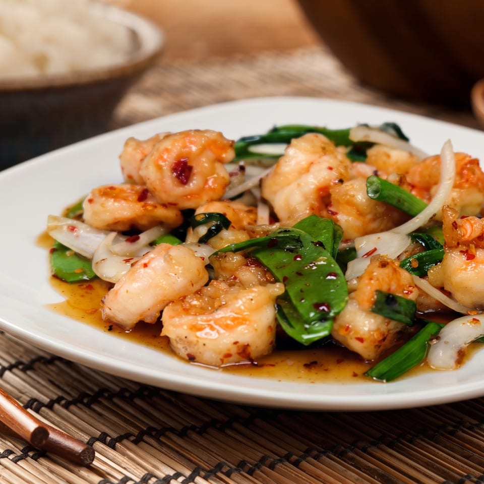 Shrimp stir-fry with green beans, onions, and chili flakes in a savory sauce on a white plate.
