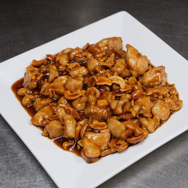A white square plate filled with cashew chicken in a rich brown sauce.