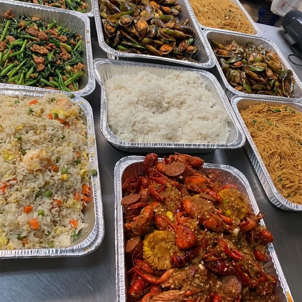 A catering spread of Asian dishes including fried rice, noodles, mussels, greens, and crawfish.