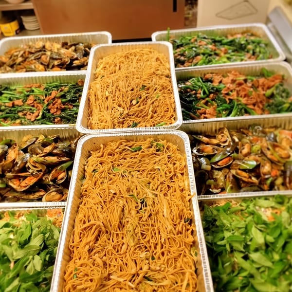 Multiple foil trays filled with noodles, mussels, and green vegetables, ready for catering.